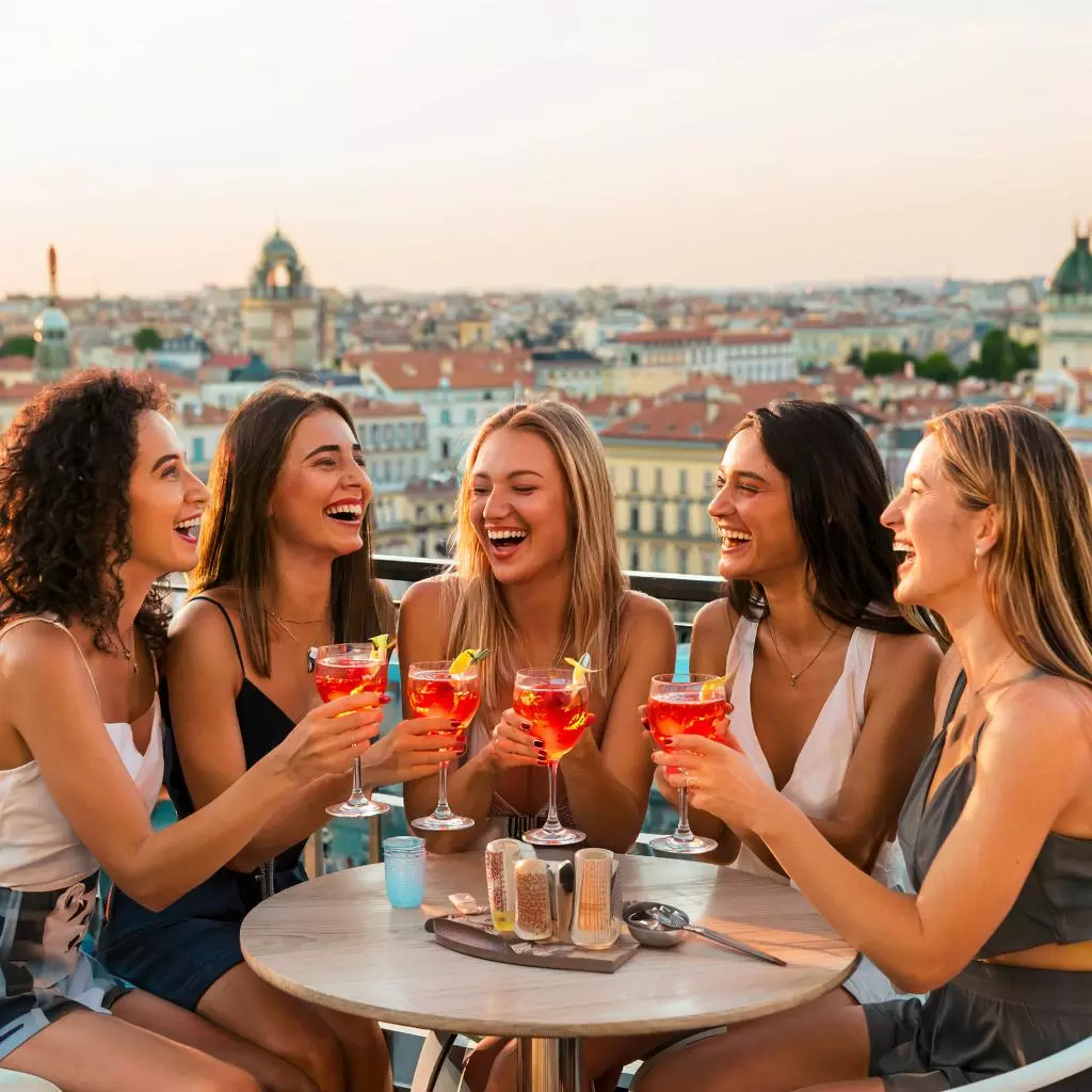 Группа друзей наслаждается Aperol Spritz на летней веранде с видом на город