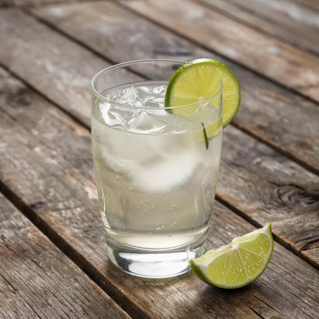 Стеклянный бокал с Lillet Blanc и лаймовой долькой на фоне деревянного стола